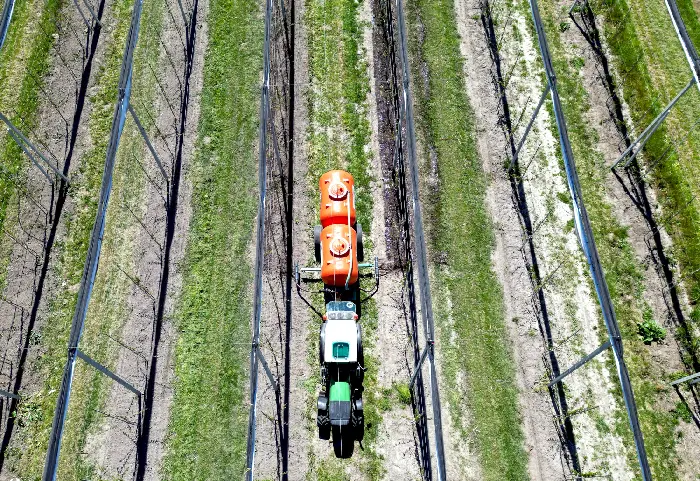 Letecký pohľad na traktor s rosičom prechádzajúci medzi riadkami výsadby